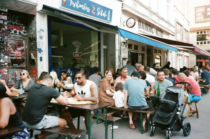 Many diners of all ages sitting outside a casual restaurant in Europe.