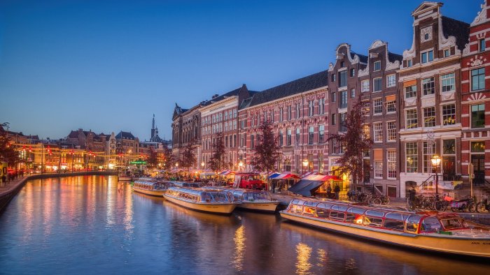 Boats docked along a canal bank in Amsterdam at night.