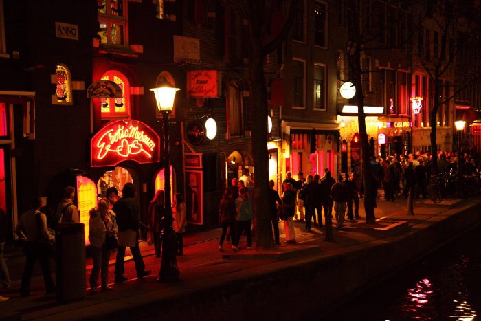 Amsterdam's Red Light District at night with crowds of people walking along the sidewalk.