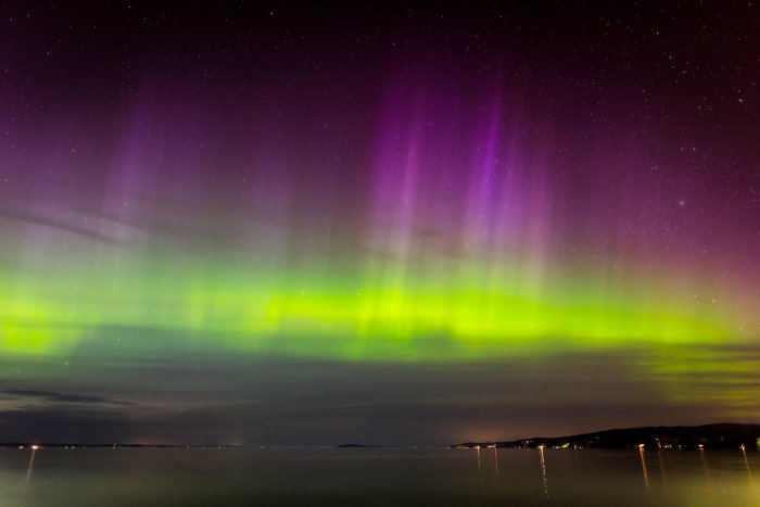 The purple and green aurora of the northern lights over a the water.