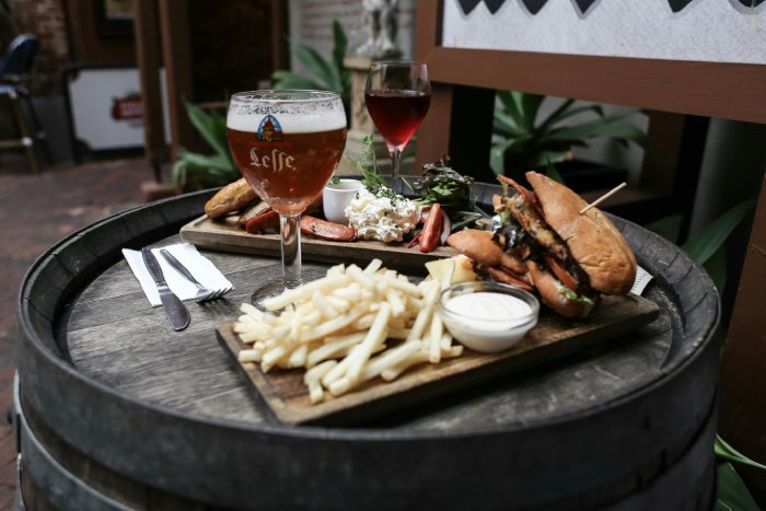 Two entrees, a beer, and a glass of wine. French fries, fancy hamburgers.