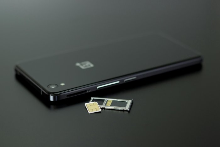 A black smartphone and a SIM card on a black surface.