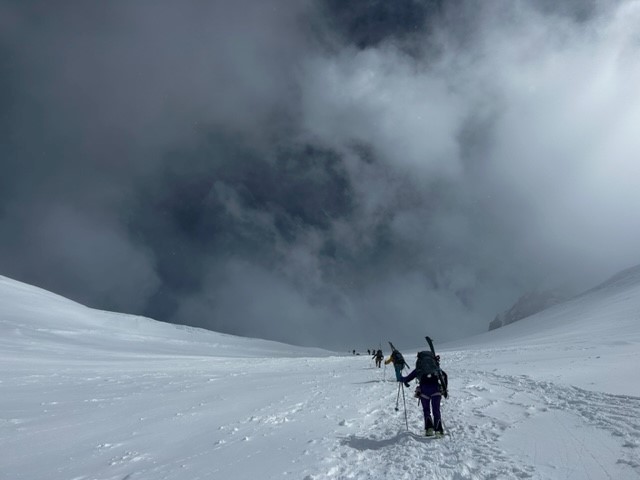 Climbers with skis on their backpacks ascend a snowy mountain,