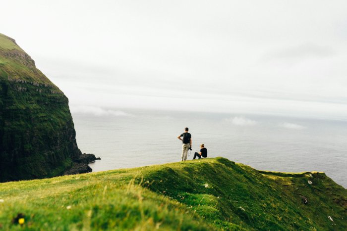 A couple atop a small point on a green, grassy oceanside cliff by the sea.