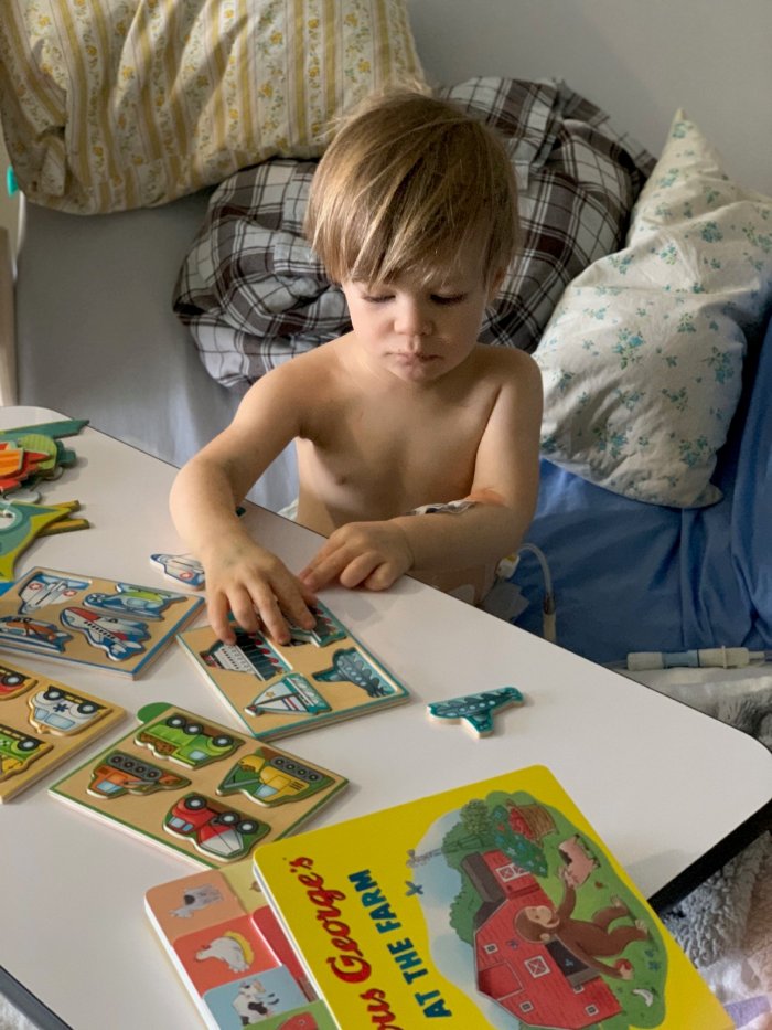 A young boy plays with a puzzle in a hospital room.