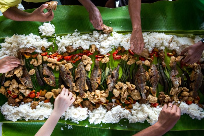 People using their hands to eat a traditional Philippines meal of rice, fish and vegetables.