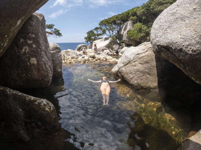 A woman floats on her back in a warm ocean pool among rocks.