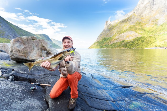 A happy man holds a fish he caught while flyfishing in Norway.