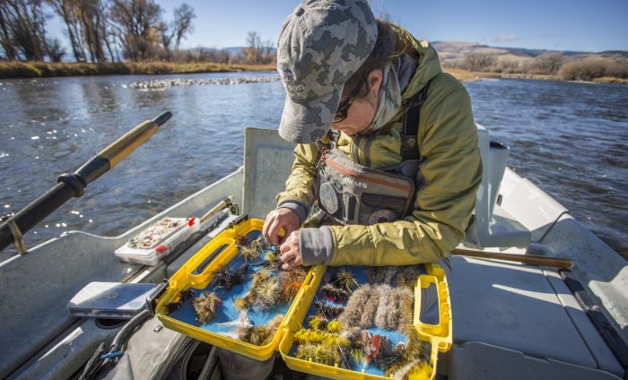 A woman chooses the right fly for flyfishing while on a small paddle boat on a cold, sunny day.