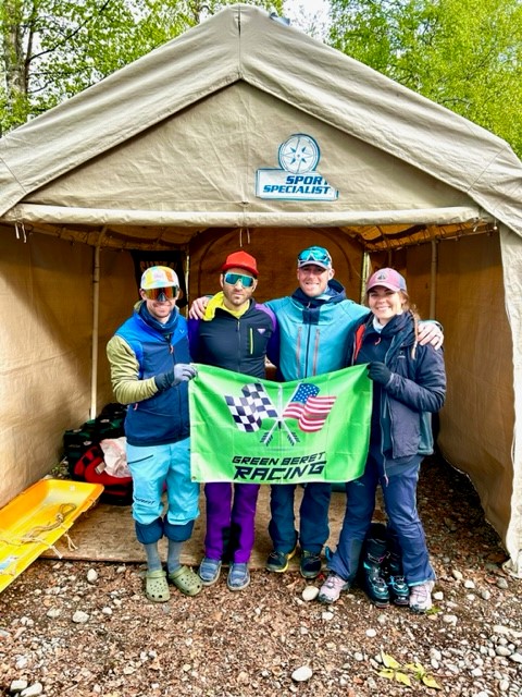 Four people hold up the Green Beret Racing flag in front of a tent.