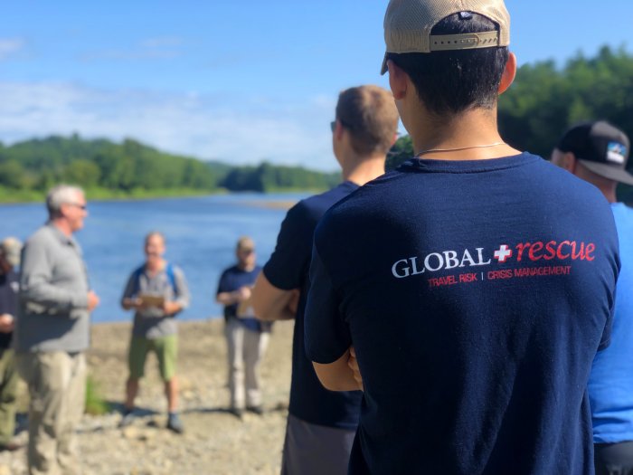 Several people listen to instruction during a training exercise near a lake on a sunny day.