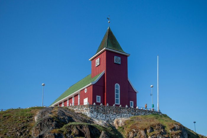 A red church with a green steeple under a blue sky in Greenland.