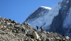 Two trekkers in Nepal walking on rocky surface with snow capped mountains