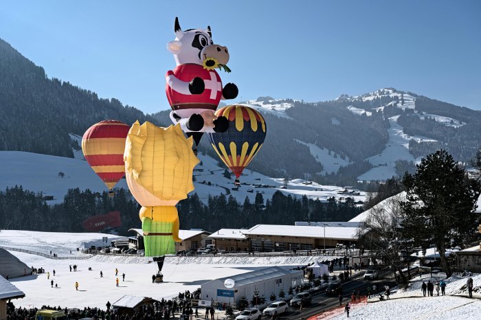 Colorful hot air balloons rise up from the bottom of a Swiss ski resort.