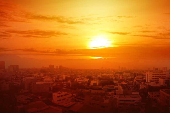 The hot orange glow of a setting sun above a hot city.