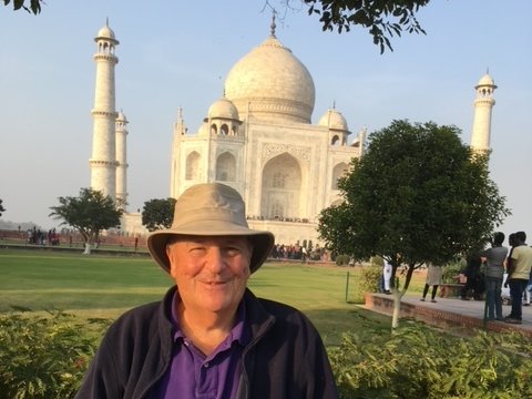 A man with a hat poses before the Taj Mahal on a sunny day.