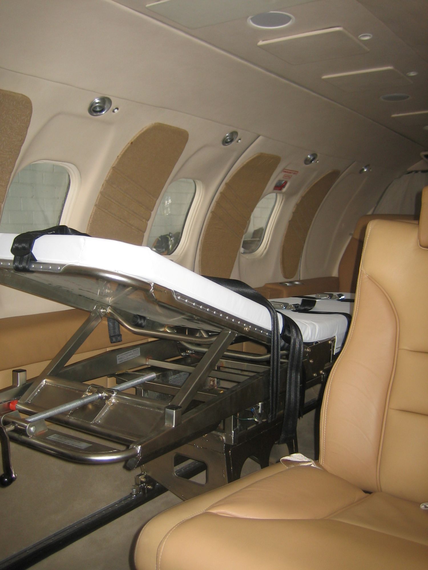 Vista interior de un avión de evacuación médica que muestra un sistema de camillas y asientos de cuero, listo para el transporte de pacientes.