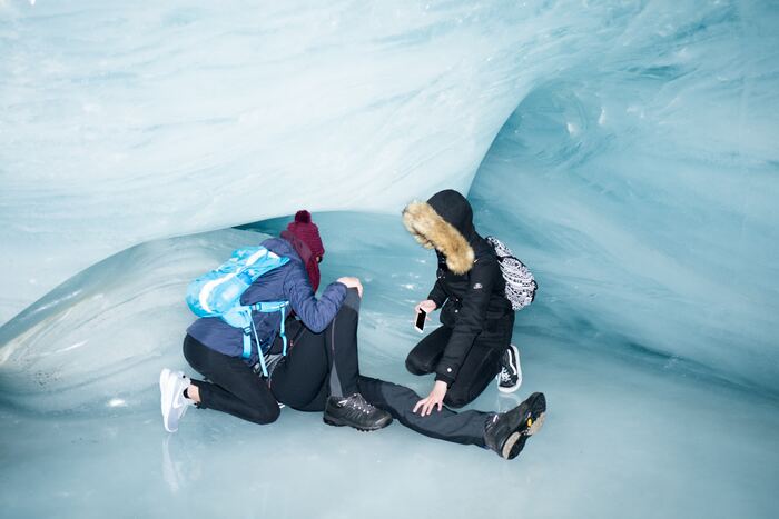 A person lying on the ice in an ice cave as two people attend to him.