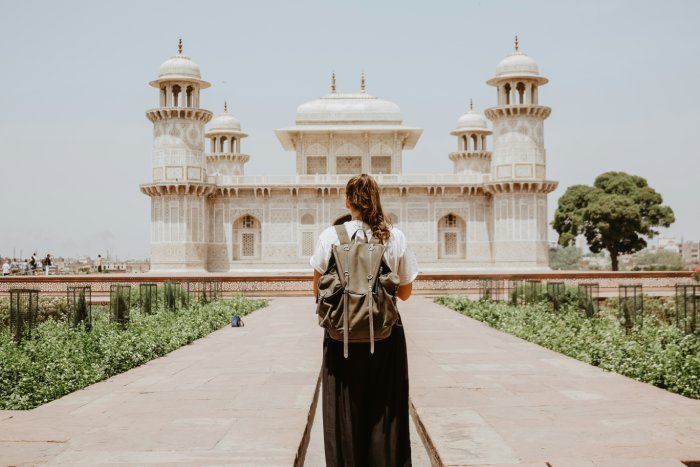 A woman wearing a backpack observes a beige temple in India.