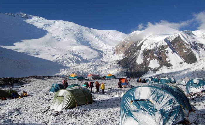 People stand around a high-altitude base camp below a snowy peak. 