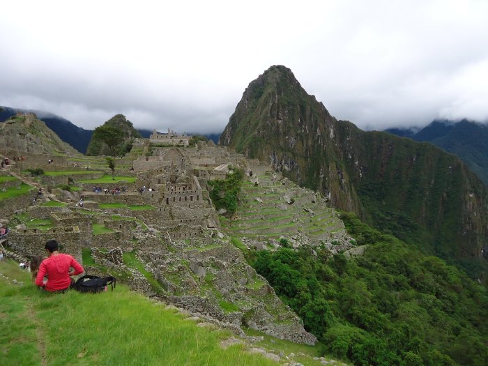 A woman sits on the grass high above Machu Picchu