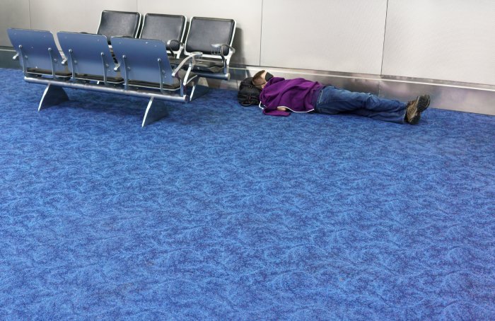 A man sleeps with a sleep mask over his eyes on an airport terminal floor.