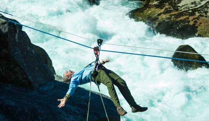 A man hangs from a rope line above a river.