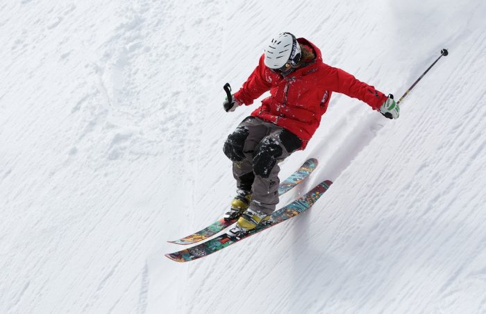 A skier in a red jacket skis powder snow on steep trail. 