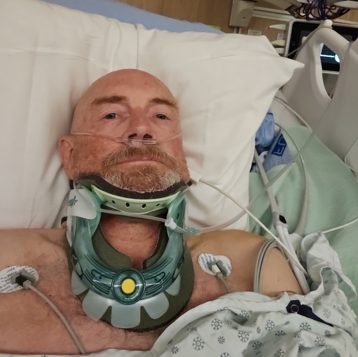 An injured man with a neck brace recovers in the ICU of a hospital.