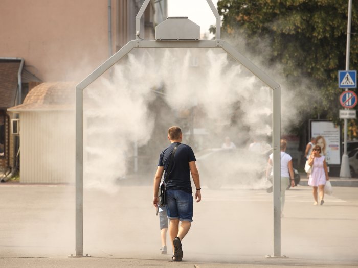 A man and young child walk through a mist machine in a city square.