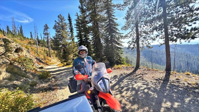 A motorcycle rider with a full-face helmet rides along a forest road in the mountains of British Columbia.