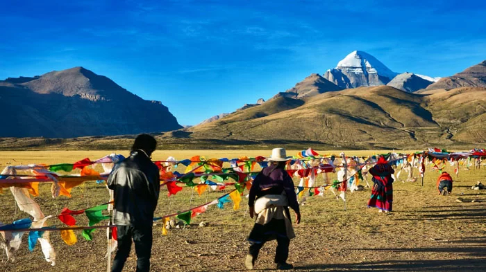 Tibetans walk along prayer flags in the plains below Mt. Kailash under clear blue skies.
