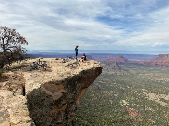 Two mountain bikers take a break on a cliffside, high above the Moab desert in Utah.