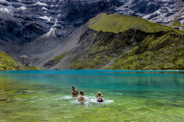 Three people swim in the clear blue waters of a mountain lake.