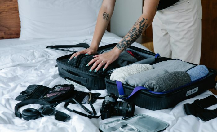 A woman with arm tattoos packs a neat suitcase with clothing and camera equipment.