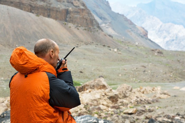 A man in an orange jacket uses a satellite phone from the mountains.