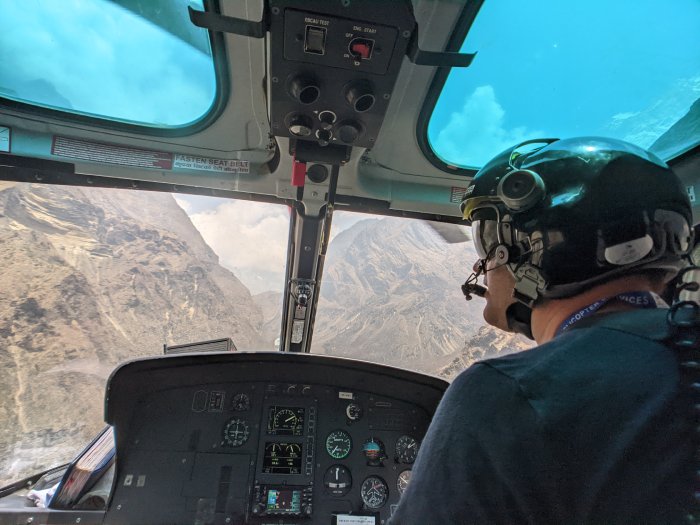 A helicopter pilot surveys the mountain terrain below from inside the cockpit.