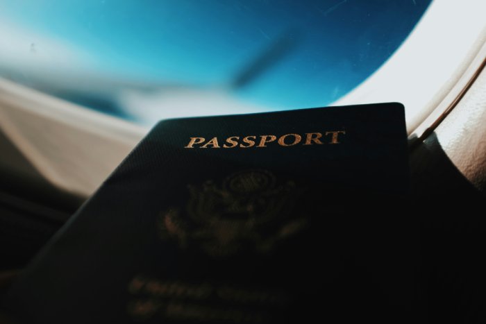 A close-up of a United States of America Passport next to a cabin window inside an airplane.