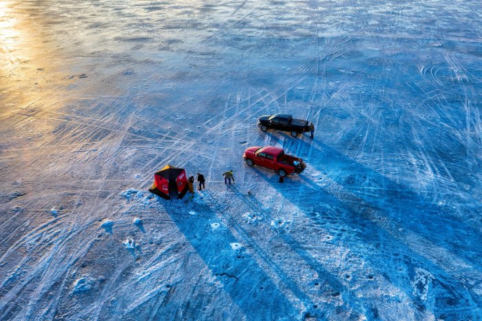 Two pick-up trucks and a shelter on the ice of a frozen lake.