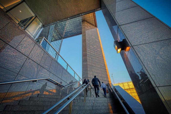 The glossy, outdoor walls and stairway of a professional building with people ascending.