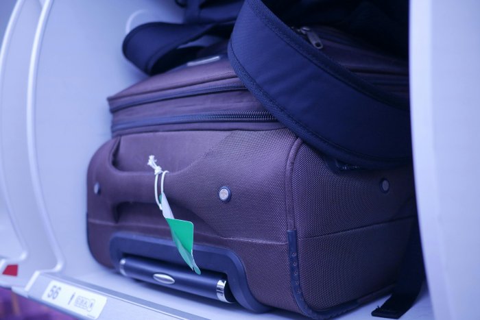 A purple carry-on suitcase stored in the overhead bin on an airplane.