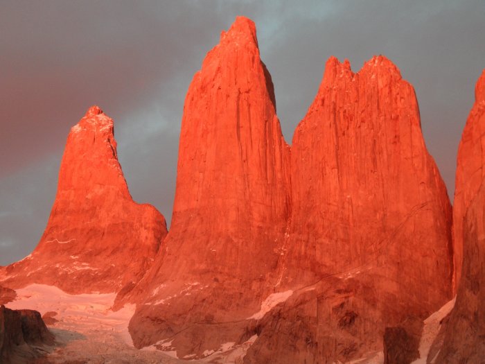 The low sun hits towering red rocky peaks in the Torres del Paine National Park.