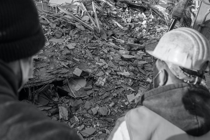 Two rescue workers look at building rubble after an earthquake.
