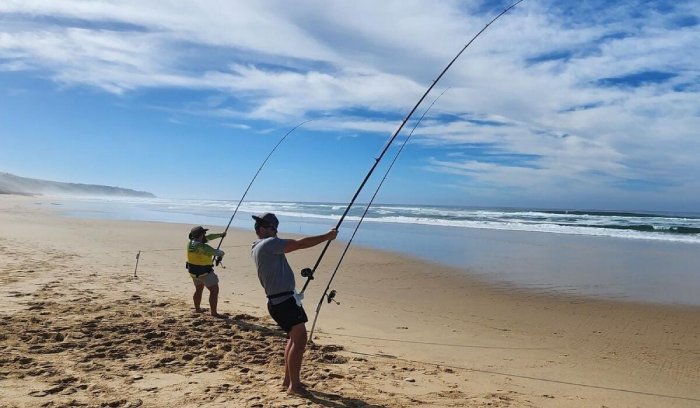 Two men grab their surfcast fishing poles while fishing on a beach.