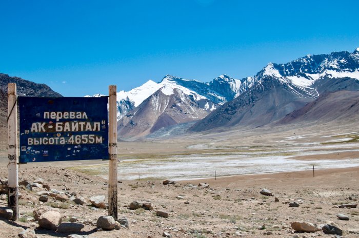 A roadside sign, a prairie, and snowy mountains under a blue sky.