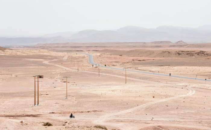 A small motorcycle rides across the sandy roads of the Moroccan desert.
