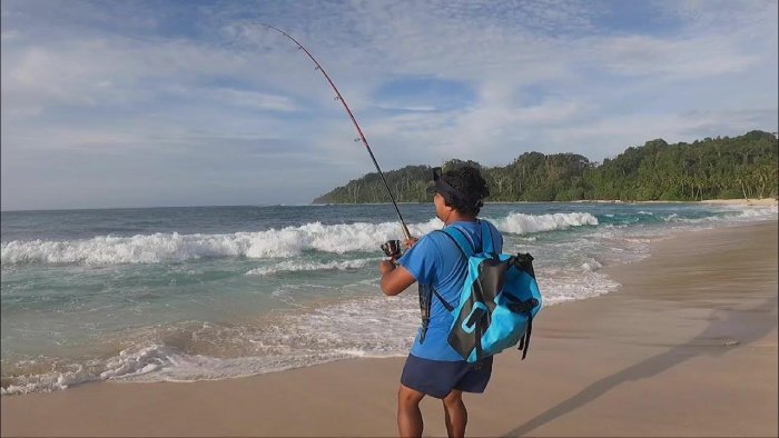 A man with a backpack surfcasts on a tropical beach in India.