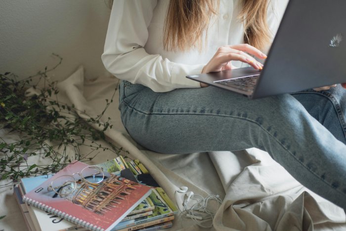 A young woman researches on her laptop computer with journals next to her.