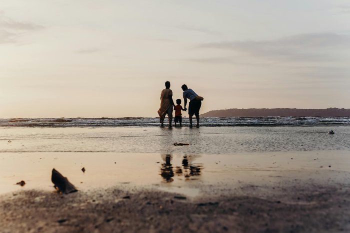 Two adults and a child on a beach at dusk during low tide.