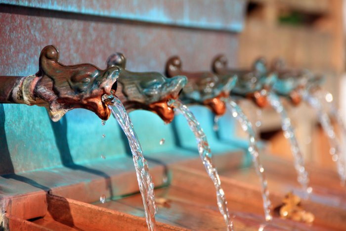 A row of ornate water fountain heads stream water into small basins.